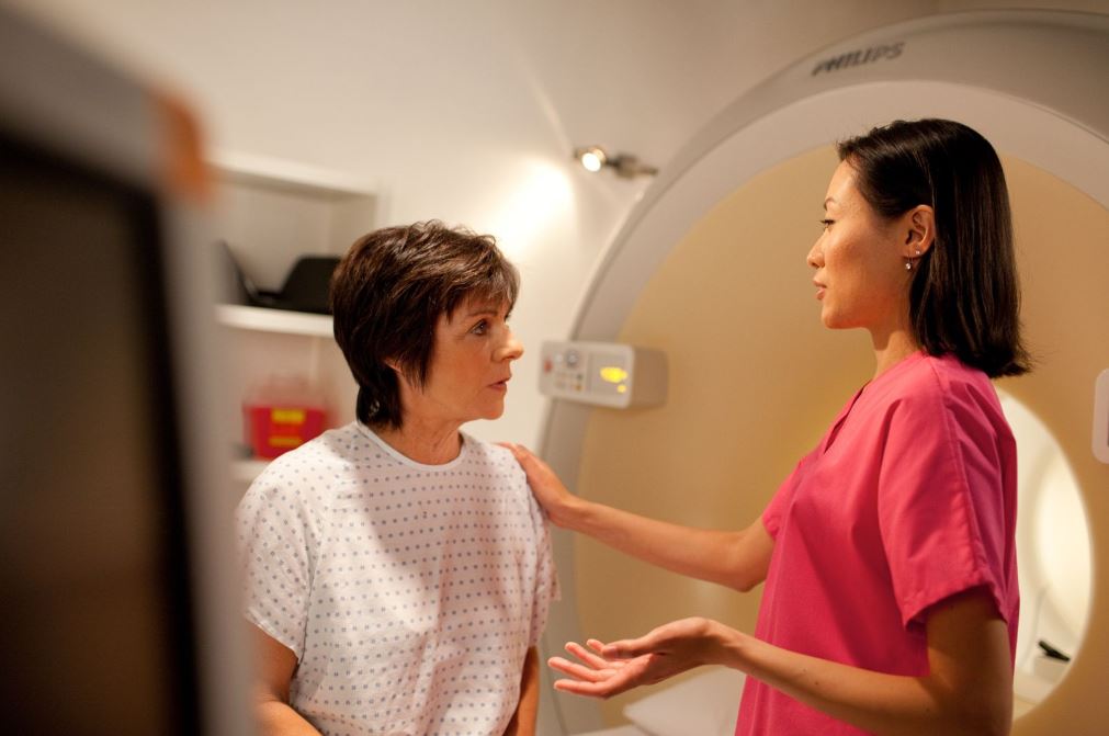 male tech in blue scrubs looking with caring eyes to a male patient wearing green in the CT scanner